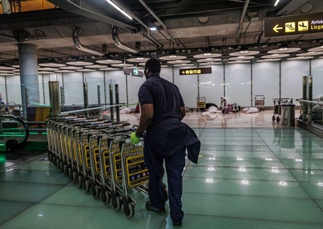 Imagen secundaria 1 - Indigentes pasan la noche en T4 de Barajas la madrugada de ayer; debajo, un trabajador recoge los carritos y una policía nacional en la planta 1