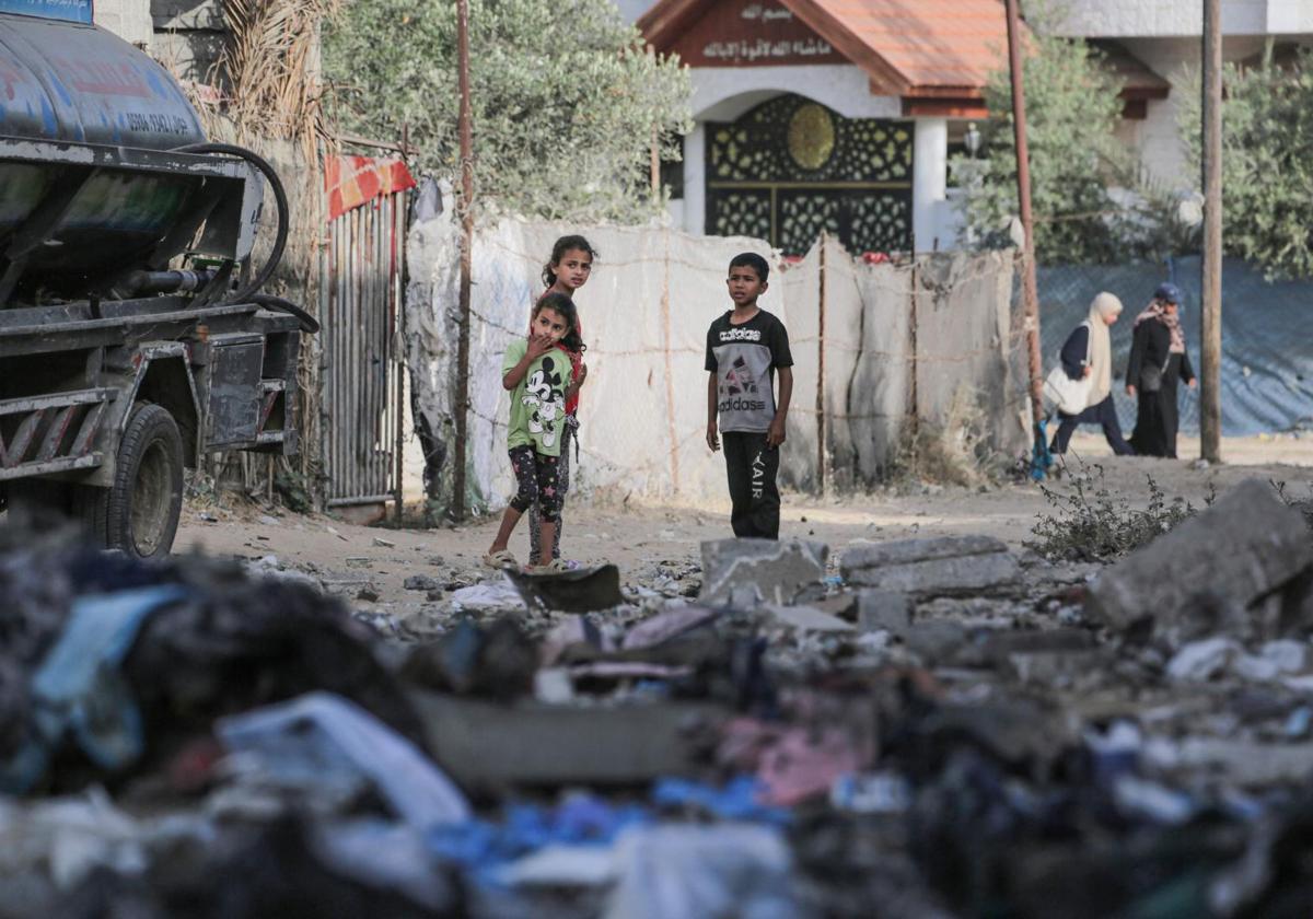 Mujeres palestinas pasan junto a niños que observan los daños causados por los bombardeos israelíes