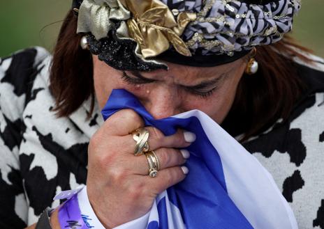 Imagen secundaria 1 - Primera foto: una mujer muestra una imagen de los rehenes israelíes en manos de Hamás. Una mujer llora durante la Marcha de los Vivos en la segunda imagen. En la última, personas caminan con banderas de Israel a la espalda durante la Marcha de los Vivos